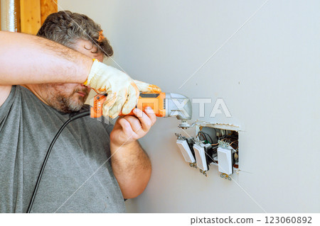 Construction worker repairs electrical light switches in home, precise tool operation safety. 123060892