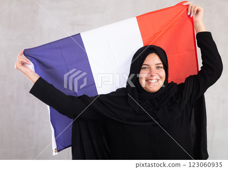 Balanced smiling Muslim woman in traditional black hijab holds flag of France Balanced smiling Muslim woman in traditional black hijab holds flag of France 123060935