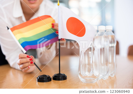 Rainbow flag and flag of Japan in female hands on negotiating table 123060940