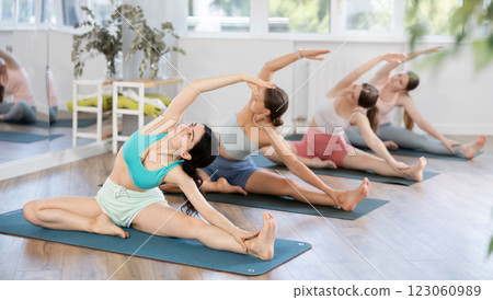 Women exercising Hatha yoga in fitness studio, sitting on mat and doing stretching in Parivrtta Janu Sirsasana Women exercising Hatha yoga in fitness studio, sitting on mat and doing stretching in Parivrtta Janu Sirsasana 123060989