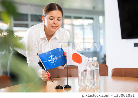 Positive young woman putting little flag of NATO on table next to the flag of Japan 123061051