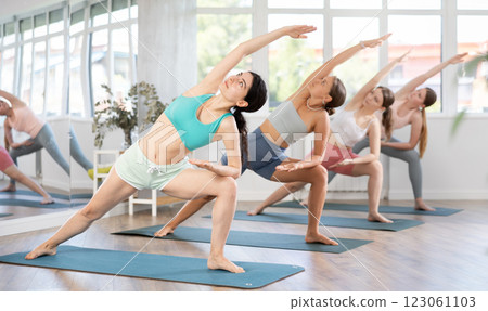 Young girl teaches yoga lesson, shows students technique of performing Utthita Parshvakonasana asana Young girl teaches yoga lesson, shows students technique of performing Utthita Parshvakonasana asana 123061103