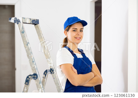Portrait of contented young female builder in blue overalls during the repair of cottage 123061130