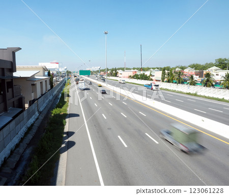 A busy highway with vehicles in motion, surrounded by buildings and greenery A busy highway with vehicles in motion, surrounded by buildings and greenery 123061228
