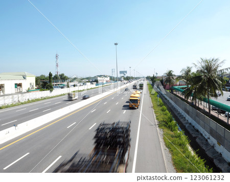 A busy highway scene with vehicles in motion, surrounded by greenery and buildings. clear blue sky adds to vibrant atmosphere 123061232