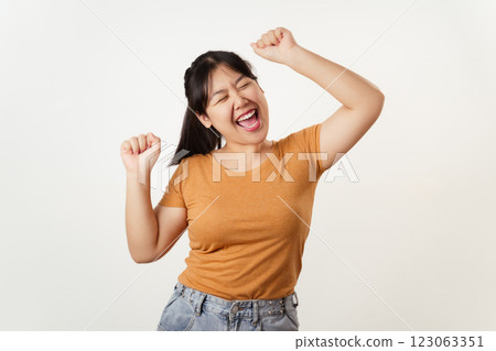 A young woman in casual clothes raising her arms, smiling, laughing with joy, cheerful emotion. 123063351