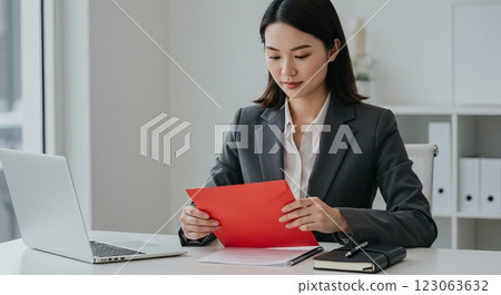 Businesswoman in suit reading document at desk with laptop and notebooks Businesswoman in suit reading document at desk with laptop and notebooks 123063632