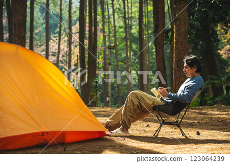 solo traveler in nature concept with asian man camping and work online with pink cherry blossom and pine tree in springtime season 123064239
