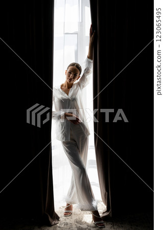 Bride opening curtains in white silk pajamas on wedding day Bride opening curtains in white silk pajamas on wedding day 123065495