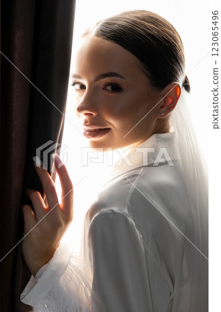 Bride wearing white suit and veil looking out the window between curtains Bride wearing white suit and veil looking out the window between curtains 123065496