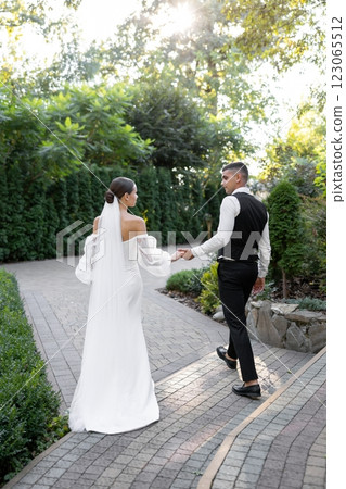 Groom tenderly embracing bride while holding hands in park during wedding ceremony Groom tenderly embracing bride while holding hands in park during wedding ceremony 123065512