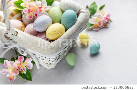 Pastel colored easter eggs overflowing from a white wicker basket decorated with spring flowers Pastel colored easter eggs overflowing from a white wicker basket decorated with spring flowers 123066652