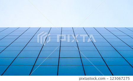A minimalist perspective of a modern glass facade, capturing the perfect symmetry of blue-tinted windows stretching towards a clear, pale sky 123067275