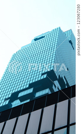 A modern high-rise building with a blue-tinted glass facade, featuring stacked and protruding sections that create a dynamic architectural form A modern high-rise building with a blue-tinted glass facade, featuring stacked and protruding sections that create a dynamic architectural form 123067280