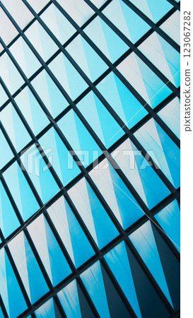A geometric glass facade with a repeating pattern of blue-tinted triangular panels, creating a modern and dynamic architectural aesthetic A geometric glass facade with a repeating pattern of blue-tinted triangular panels, creating a modern and dynamic architectural aesthetic 123067282