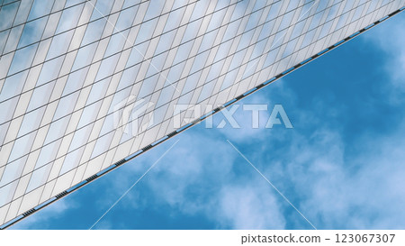 A sleek, angled building with a reflective, grid-like glass facade dominates the left, contrasting against a vibrant blue sky with soft white clouds. 123067307