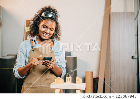 Carpenter woman in a workshop uses her smartphone. Business owner and product designer managing projects online, reviewing designs, and gathering feedback for evaluation and improvement 123067943
