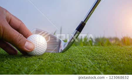 Hand-wearing golf glove holding a white golf ball on green background Hand-wearing golf glove holding a white golf ball on green background 123068632