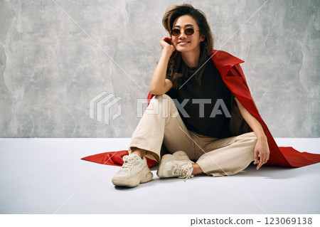 Fashionable smiling woman wearing red coat and stylish casual outfit posing at studio. 123069138