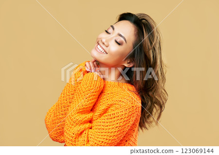 Pretty asian woman in fashionable orange sweater posing on studio background 123069144