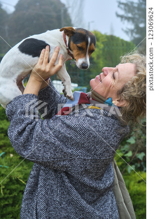 Happy senior woman holding her jack russell terrier in a garden Happy senior woman holding her jack russell terrier in a garden 123069624