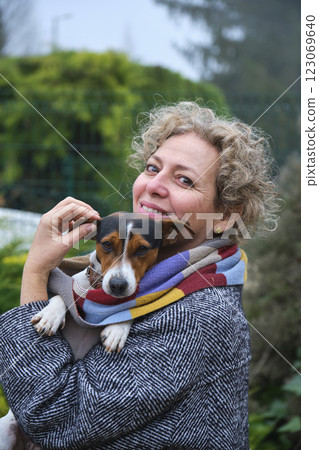 Smiling woman holding small dog wrapped in scarf outdoors 123069640
