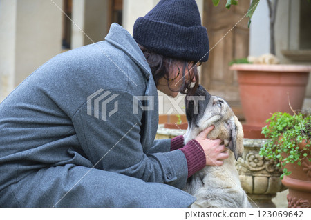 Young woman wearing beanie lovingly kissing puppy in courtyard 123069642