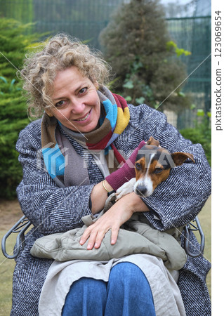 Smiling woman holding small dog on lap in garden setting 123069654