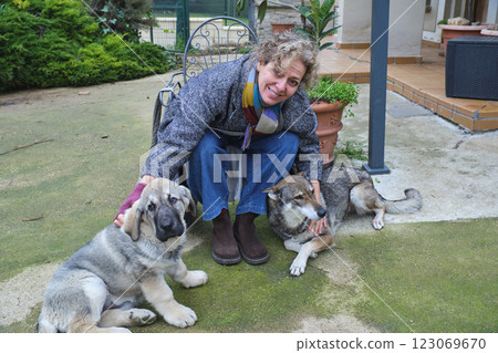 Happy woman petting two puppies in a garden Happy woman petting two puppies in a garden 123069670