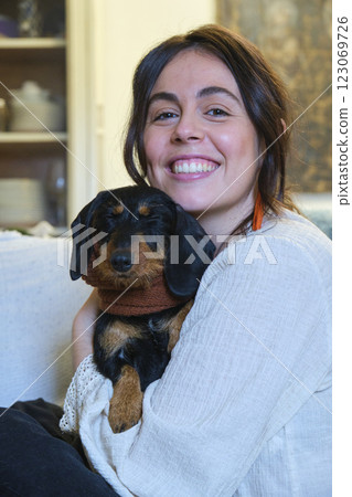 Smiling woman hugging her cute miniature wire-haired dachshund at home Smiling woman hugging her cute miniature wire-haired dachshund at home 123069726
