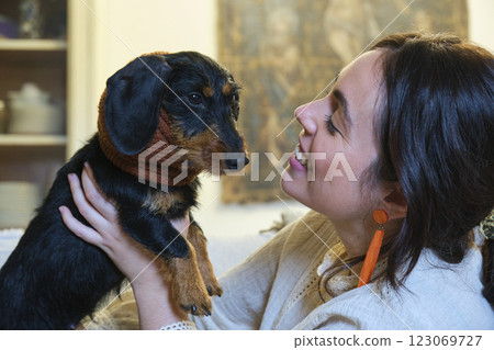 Smiling woman holding her adorable wire-haired dachshund wearing ear warmers 123069727