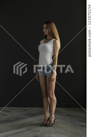 young woman in a white tank top and denim shorts on a dark background, full length portrait young woman in a white tank top and denim shorts on a dark background, full length portrait 123070154