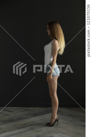 young woman in a white tank top and denim shorts on a dark background, full length portrait young woman in a white tank top and denim shorts on a dark background, full length portrait 123070156