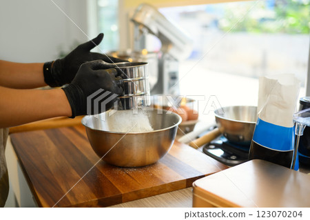 Young man sifting flour for homemade cookies in a bright kitchen Young man sifting flour for homemade cookies in a bright kitchen 123070204