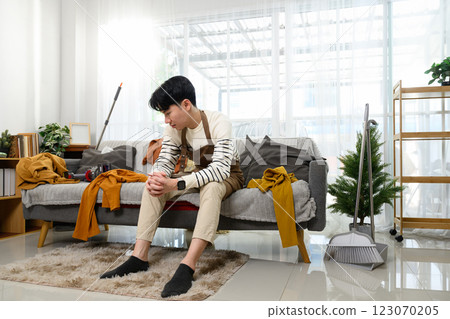 Tired man sitting on the couch, takes a break from house cleaning Tired man sitting on the couch, takes a break from house cleaning 123070205