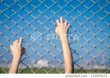 Closeup of a human hand gripping a chain link fence as if trying to escape, representing border control, imprisonment, human trafficking, and the fight against restricted movement and injustice. 123070272