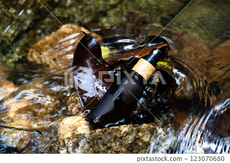 A serene bottle lies on rocks with flowing water and leaves, showcasing a natural hydration theme. 123070680