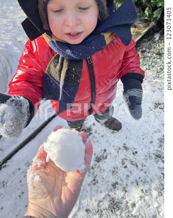 Little boy in red jacket, mittens and warm hat take snowball. Sunny day in winter. Snow and the seasons.  123071405
