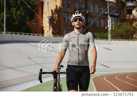 Athletic strong man cyclist wearing professional cycling garment leading bike 123071701