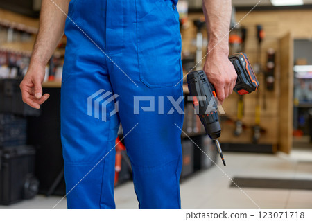 Crop portrait of repairman holding drill in hands over workshop interior Crop portrait of repairman holding drill in hands over workshop interior 123071718