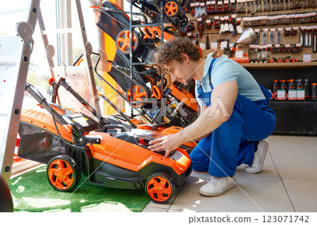 Young workman choosing electric lawnmower at garden supply store 123071742