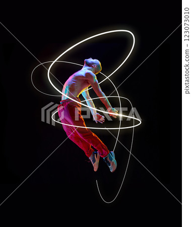 Male shirtless dancer floating mid-air, arms stretched, neon white and gold light trails spiraling around grace and strength against black background. 123073010