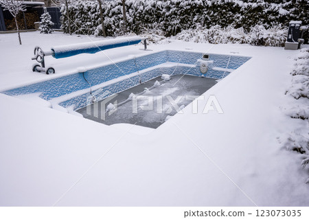 Winterized swimming pool covered in snow with protective floats preventing freeze damage. 123073035