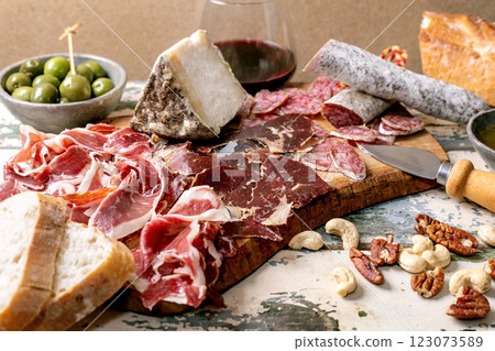 Snack board with traditional Spanish Jamon Iberico, sliced Fuet sausage, cheese, green olives, white bread, nuts, olive oil, glass of red wine. Light rustic wooden table, Closr up Snack board with traditional Spanish Jamon Iberico, sliced Fuet sausage, cheese, green olives, white bread, nuts, olive oil, glass of red wine. Light rustic wooden table, Closr up 123073589