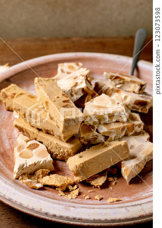 Traditional Spanish dessert classic soft orange turron and crunchy almond turron, cut into pieces on rustic clay plate with fork. Wooden table, top view. 123073598
