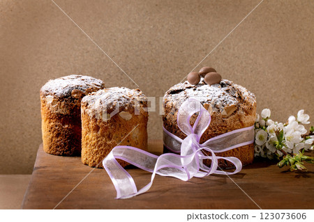 Homemade Italian traditional Easter panettone cakes in row, decorated by chocolate eggs, pink ribbon and blossoming cherry tree flowers standing on wooden table. Traditional European bake. Copy space Homemade Italian traditional Easter panettone cakes in row, decorated by chocolate eggs, pink ribbon and blossoming cherry tree flowers standing on wooden table. Traditional European bake. Copy space 123073606