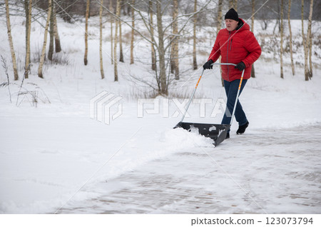 Angry man with a snow shovel cleans the pavement in the yard. Man shoveling snow after a winter storm. 123073794