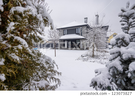 Modern two-story house with a snow-covered backyard and trees on a winter day. 123073827