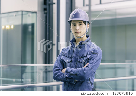 建築工地上一名年輕男工人雙手交叉，頭戴安全帽。 123073910