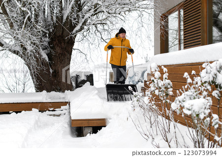 Portrait of a man in winter clothes with snow shovel cleaning snow from the terrace of the building 123073994